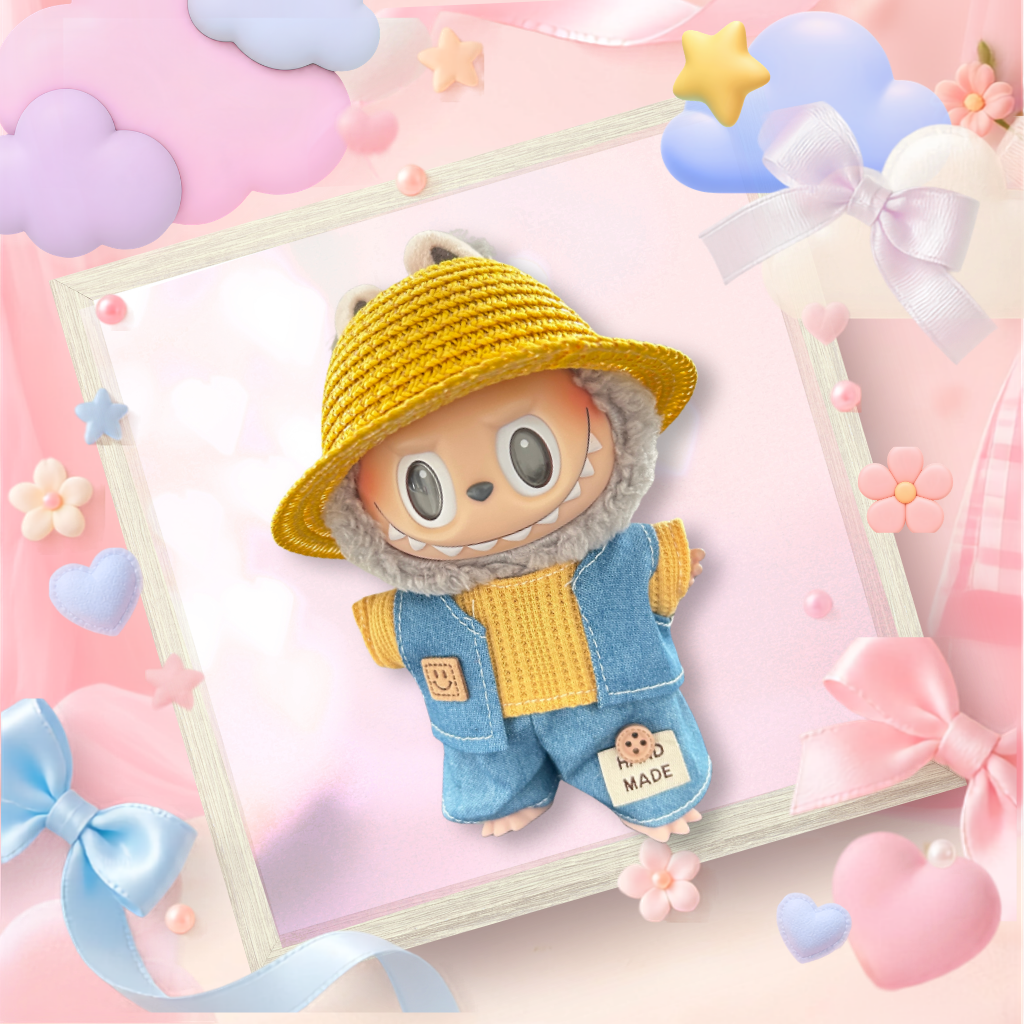 A cute plush toy character dressed in a yellow woven hat and denim overalls with a fuzzy gray hood, displayed inside a decorative white frame on a pastel pink background with bows, stars, and hearts.
