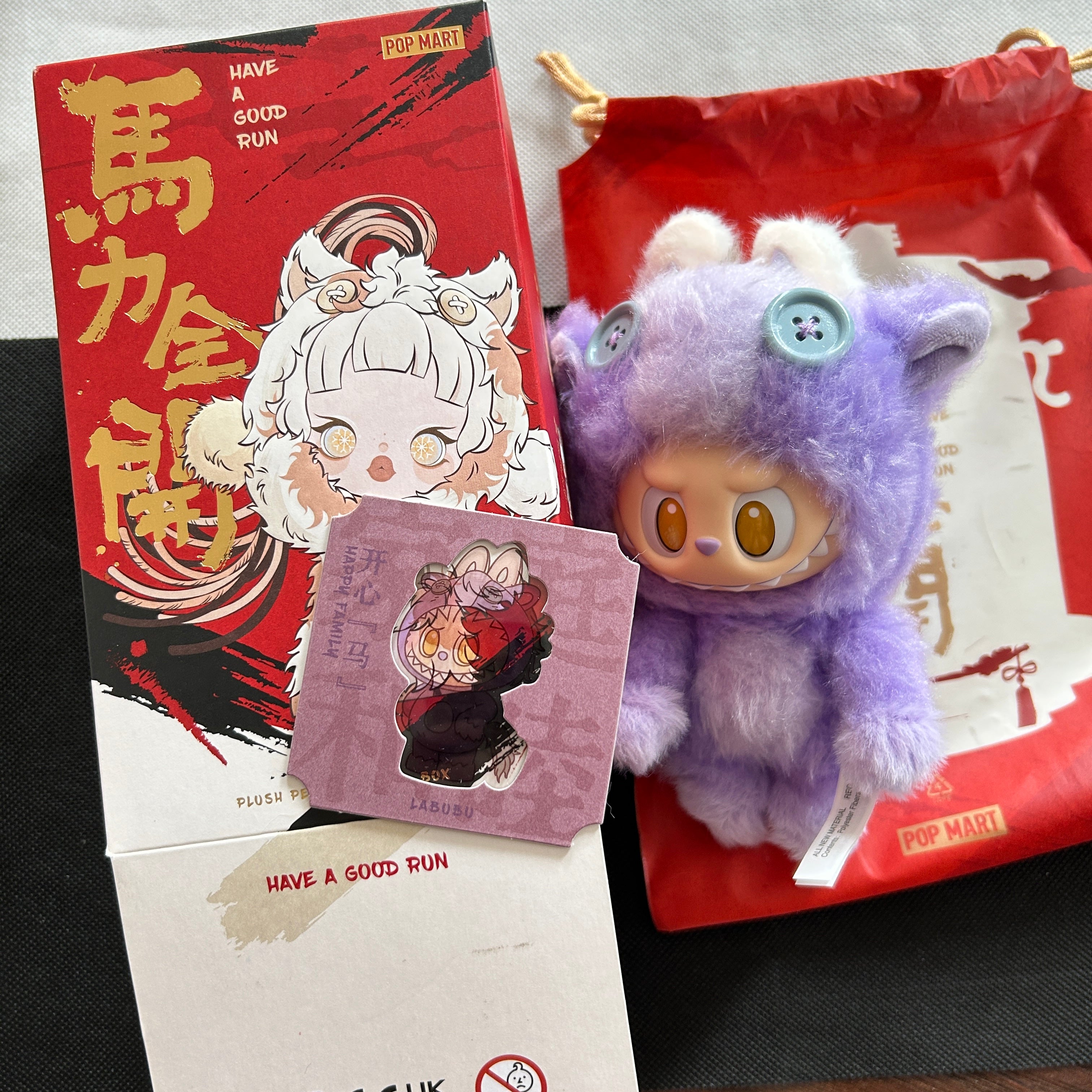 A purple Have a Good Run Series Labubu, displayed next to its red and white Pop Mart packaging box and a small card, on a dark surface.