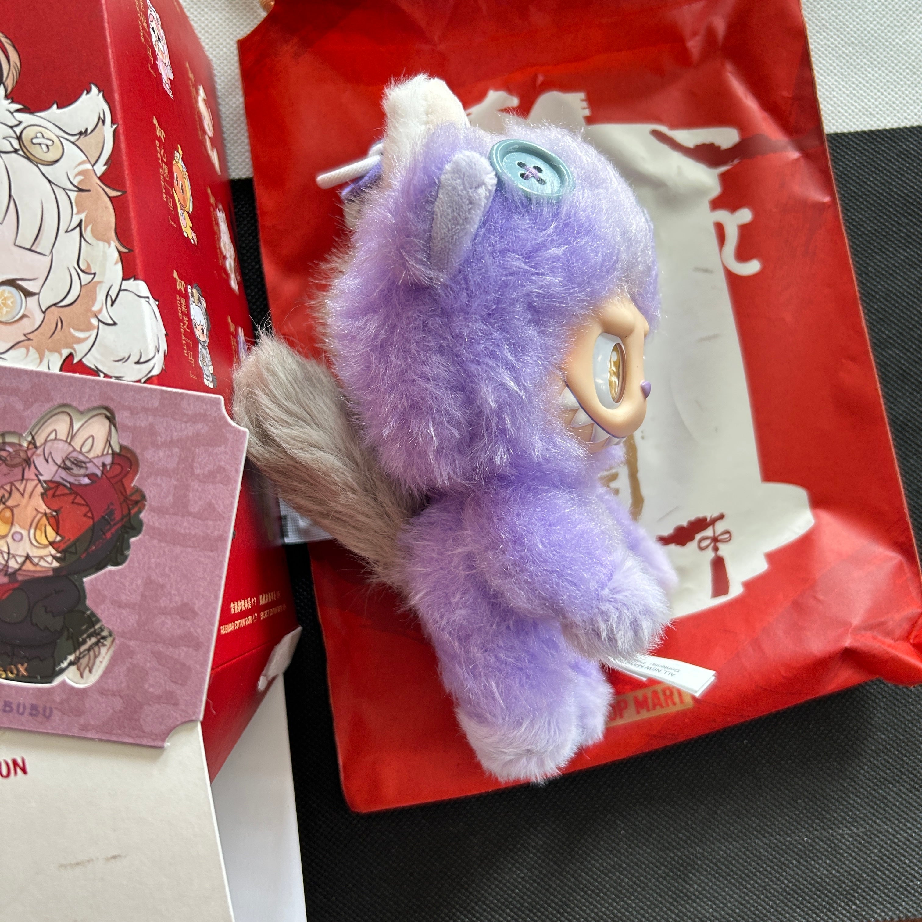 A Have a Good Run Series Labubu plush character in lavender-purple with white accents, resting on red packaging and box.