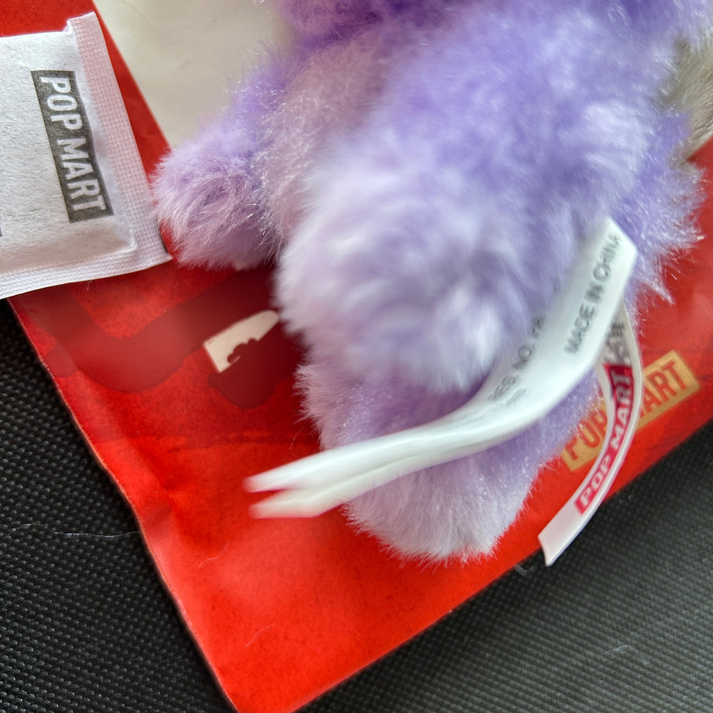 A close-up of a Labubu plush toy with a white tag reading 'MADE IN CHINA' and a small white POP MART tag.