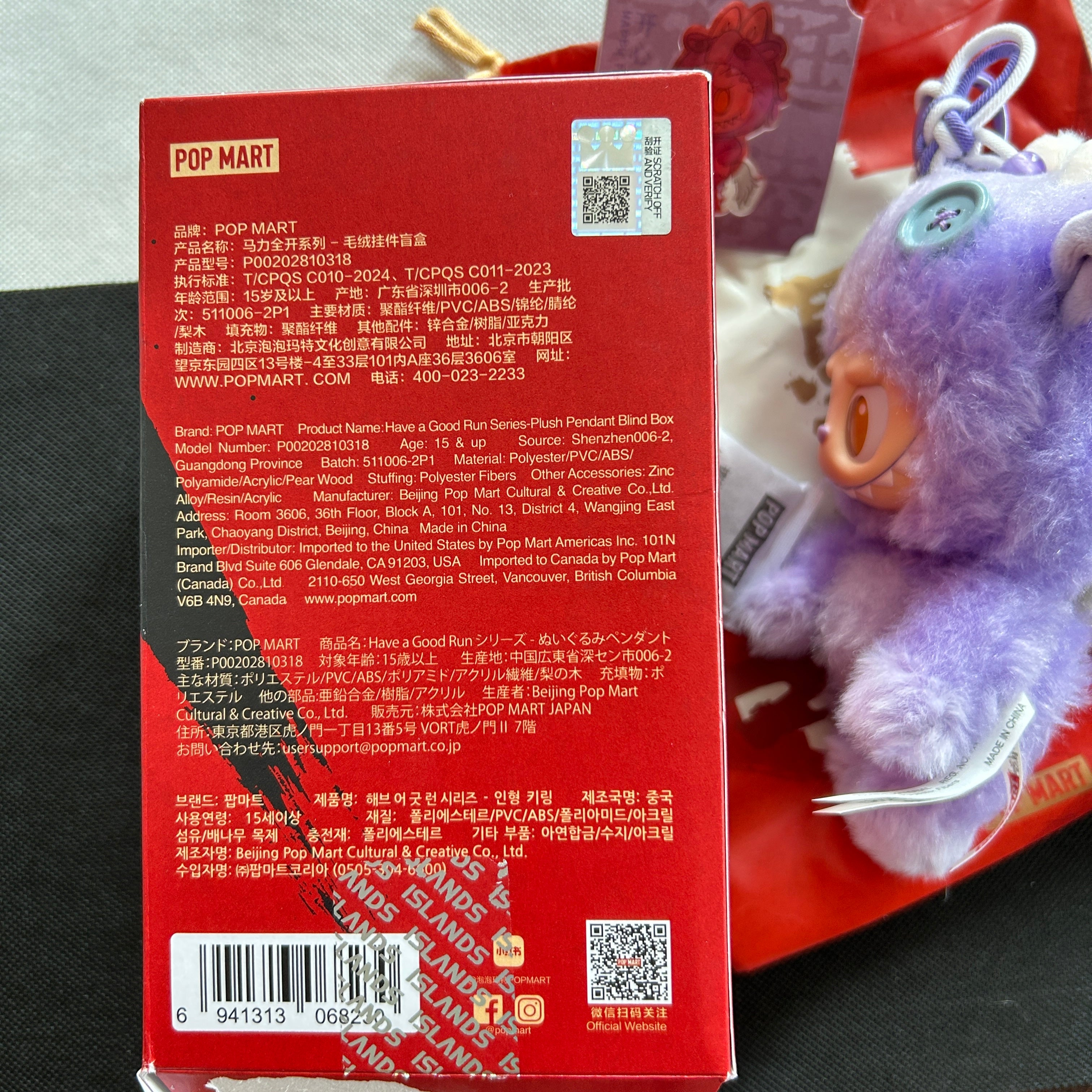 Close-up of the back of a red Pop Mart product box with printed text, barcodes, and QR codes, alongside a Labubu plush toy.
