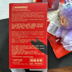 A red cardboard box with Chinese warning text and a yellow 'QC PASSED' label, photographed on a dark surface next to a small plush toy.
