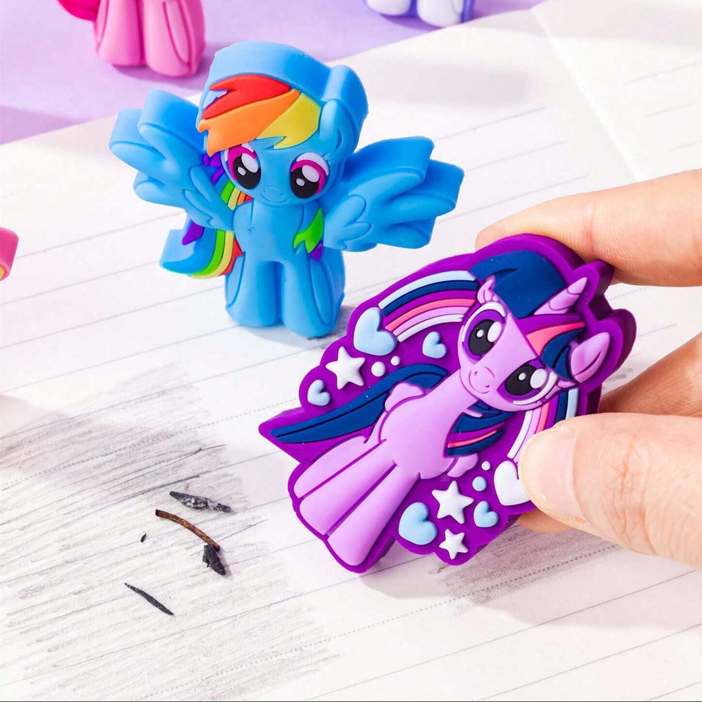 A hand holds a purple My Little Pony character eraser shaped like Twilight Sparkle, with other colorful pony character erasers resting on lined paper against a light purple background.