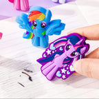 A hand holds a purple My Little Pony character eraser shaped like Twilight Sparkle, with other colorful pony character erasers resting on lined paper against a light purple background.