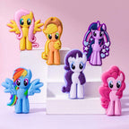 Six My Little Pony character figurines displayed on white step risers against a soft pink background. The characters include Flory Meow, Applejack, Twilight Sparkle, Rainbow Dash, Rarity, and Pinkie Pie.