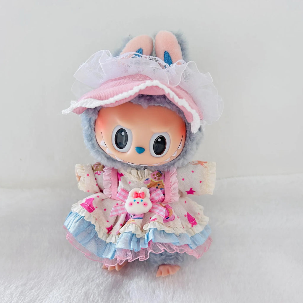 A cute plush doll with a gray bunny hood, large cartoon eyes, and a pink and blue ruffled dress with a matching pink bonnet, photographed against a soft white background.