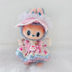 A cute plush doll with a gray bunny hood, large cartoon eyes, and a pink and blue ruffled dress with a matching pink bonnet, photographed against a soft white background.