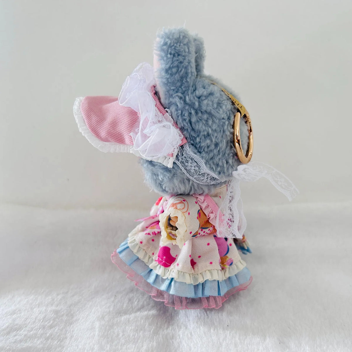 A Labubu plush doll wearing a ruffled dress in pastel pink, blue, and cream with cartoon print.  