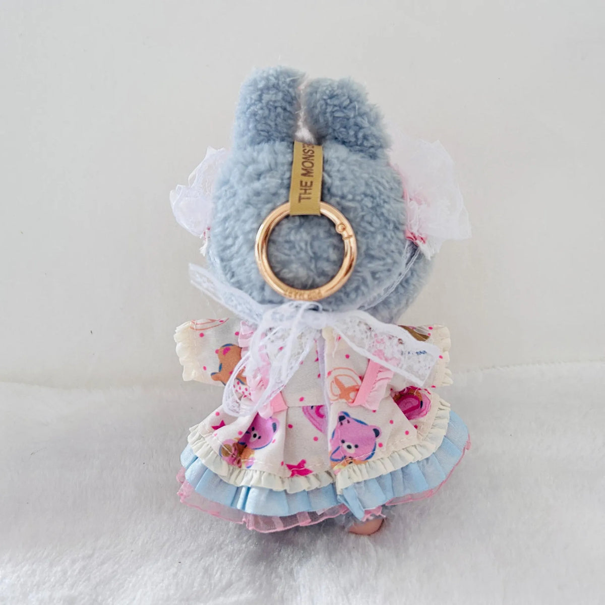 Back view of a Labubu plush doll wearing a ruffled dress with pink cartoon bear prints, white lace trim.