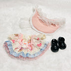 A doll outfit set featuring a pink and blue ruffled dress with a bunny applique, a pink lace-trimmed undergarment, and a pair of black doll shoes.