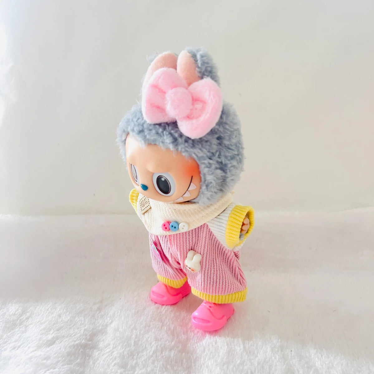 A Labubu doll wearing a large pink bow, and a pink striped outfit with yellow trim.