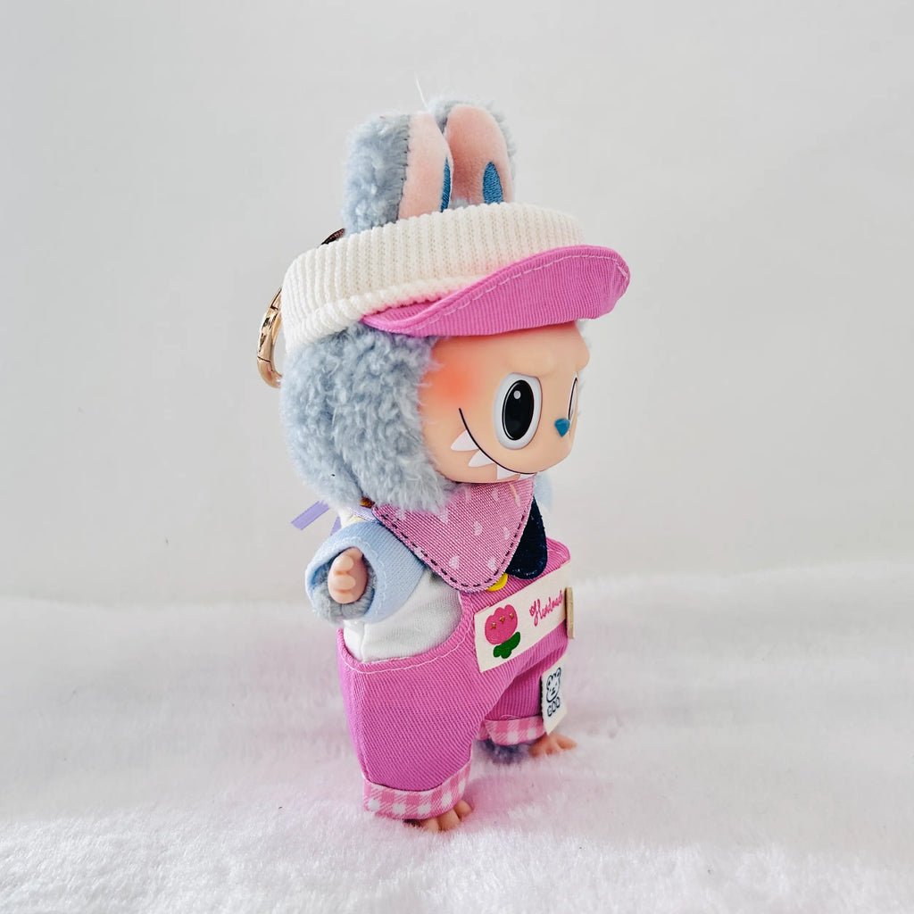A Labubu plush doll wearing a white visor with pink trim, and pink bib with a pink overalls.