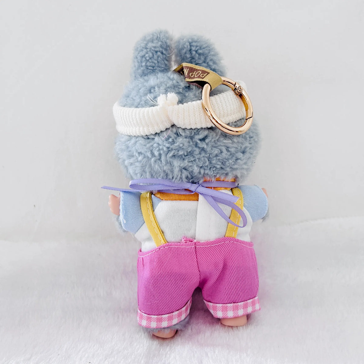 Back view of a Labubu plush doll wearing a white top and pink overalls.