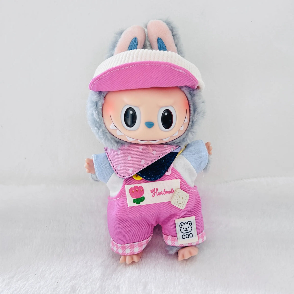 A Labubu plush doll wearing a pink visor, and pink overalls with decorative patches.