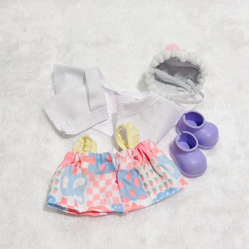 A doll outfit set back view, including a white top, a pink and blue patterned skirt, a hat and a pair of purple booties.