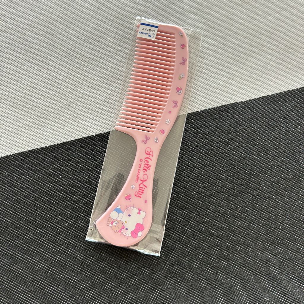 A pink Hello Kitty hair comb with rhinestone accents and a Hello Kitty illustration on the handle, shown inside a clear plastic packaging.