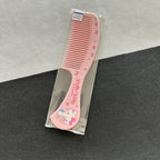 A pink Hello Kitty hair comb with rhinestone accents and a Hello Kitty illustration on the handle, shown inside a clear plastic packaging.