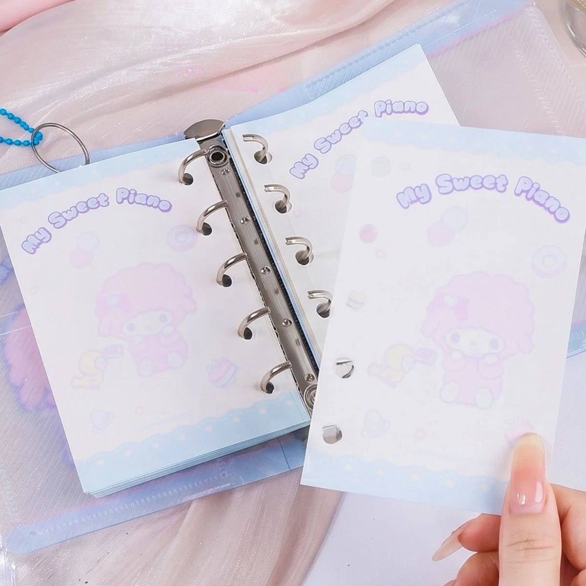 A close-up of a pastel ring binder with cute cartoon notepad pages. A hand is holding one page in front of another that is inserted into the binder.