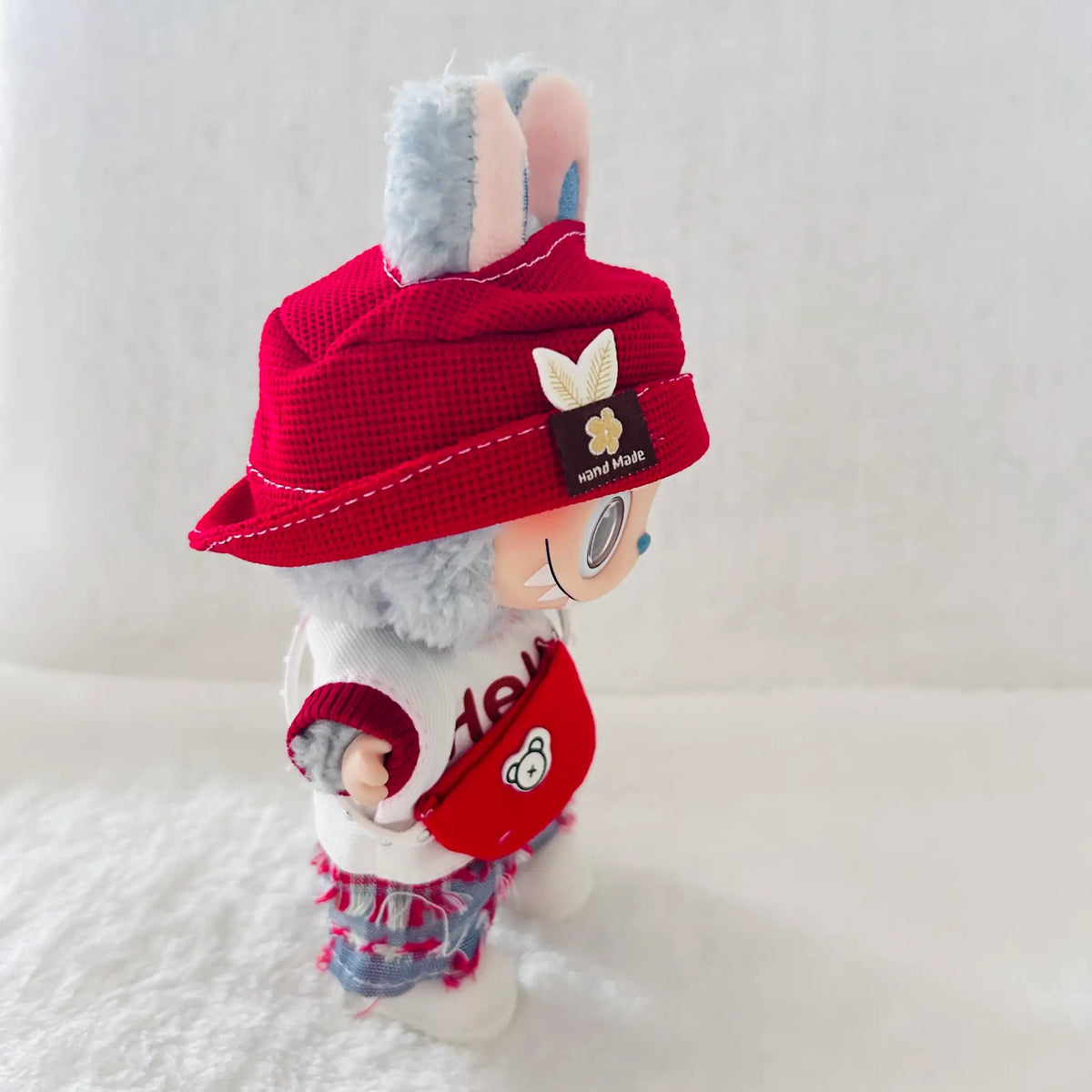 A plush wearing a red bucket hat with a small butterfly patch and a black sewn-in tag reading 'wool rabbit', a white top, and red denim shorts.