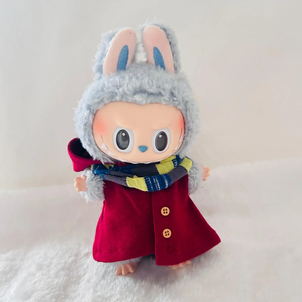 A Labubu doll wearing a bright red hooded coat with buttons and a blue, yellow, and white striped scarf.