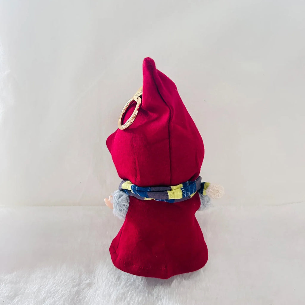 Back view of a Labubu wearing a bright red pointed hat cape, with a blue and yellow patterned scarf.
