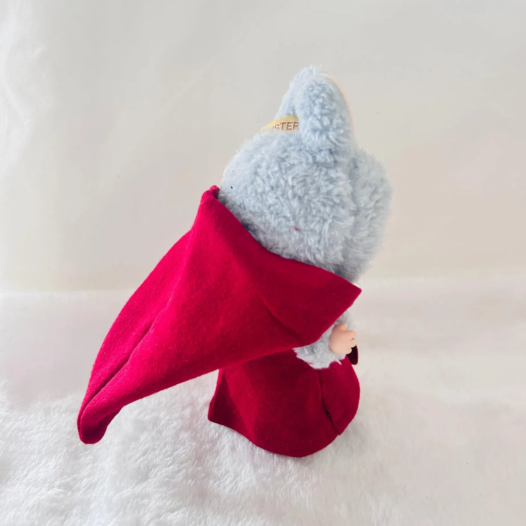 A Labubu plush toy wearing a bright red cape, posed on a soft white textured surface.