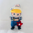A Labubu plush doll dressed in a outfit, featuring a yellow knit visor, blue denim-style overalls, a navy and white striped shirt, and black shoes. 