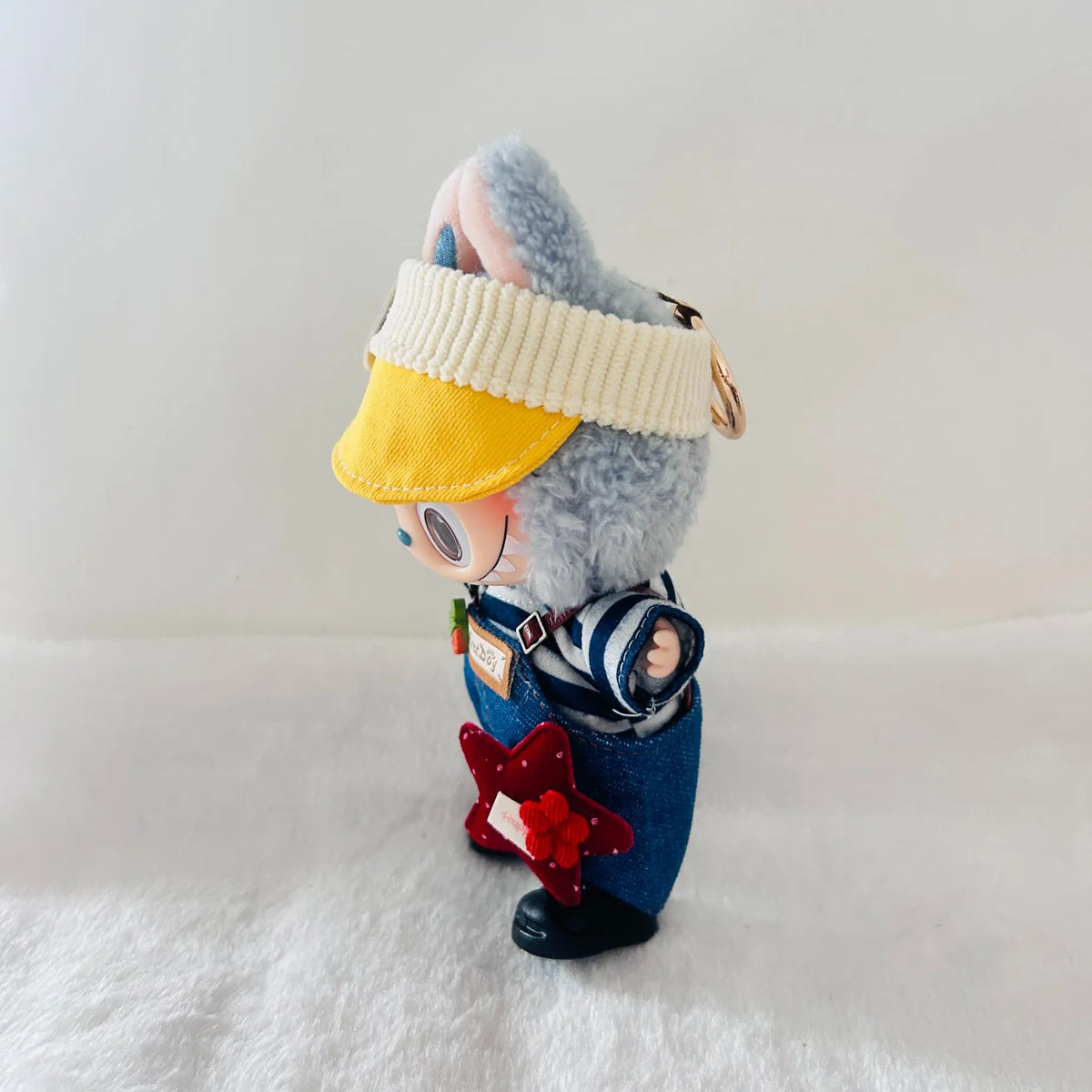 A Labubu plush toy wearing a blue denim-style overalls, a striped shirt, and a red star accessory.