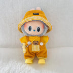 A collectible plush doll with a gray furry body, wearing a yellow corduroy outfit, a yellow and white gingham bucket hat, and yellow boots.