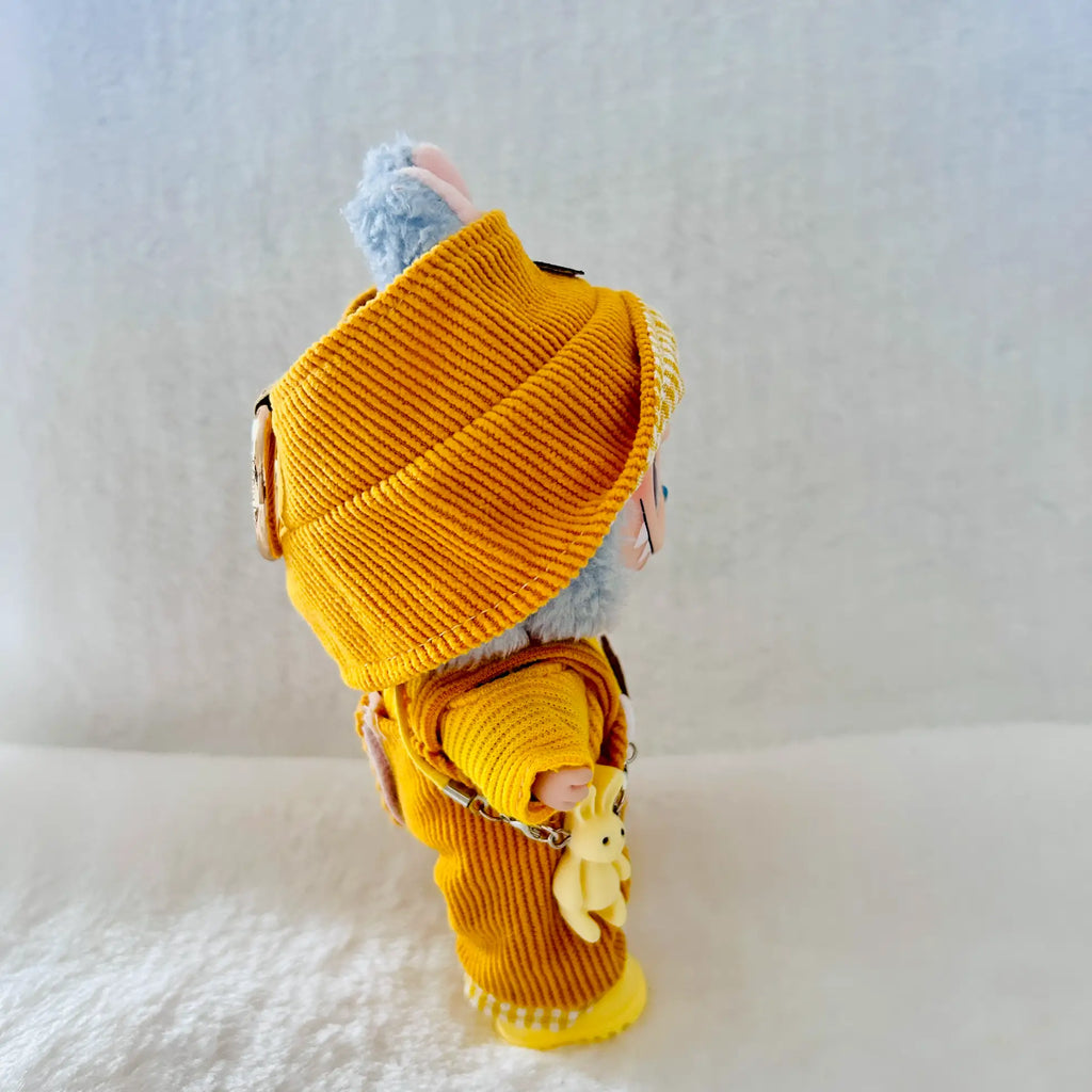 A small plush toy or doll dressed in a mustard yellow ribbed knit outfit and matching hat.