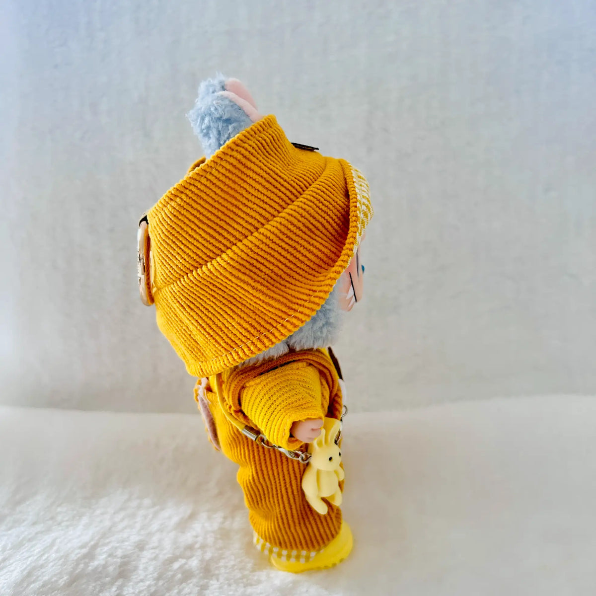 A small plush toy or doll dressed in a mustard yellow ribbed knit outfit and matching hat.