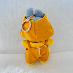 A plush bunny toy shown from the back, wearing a mustard yellow corduroy jumpsuit with blue fluffy ears and a gold metal key ring accessory attached.
