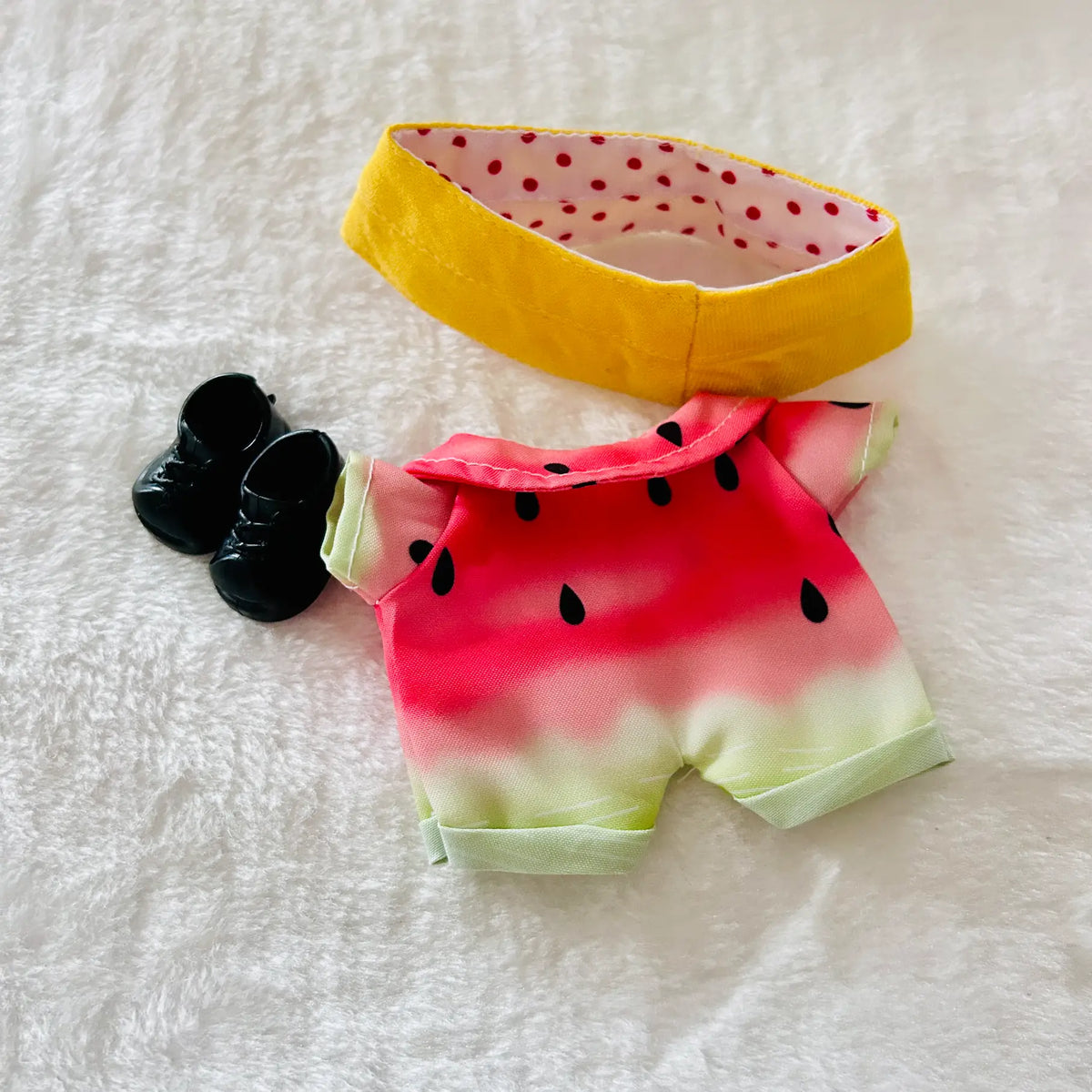 A doll outfit set featuring a watermelon-print short-sleeve romper, a yellow polka-dot headband, and small black shoes.