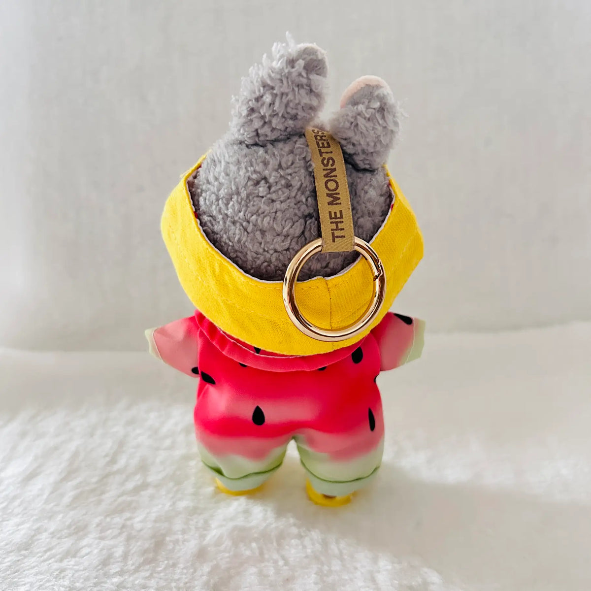 A plush gray bunny keychain or bag charm wearing a yellow headband and a pink watermelon-print outfit.